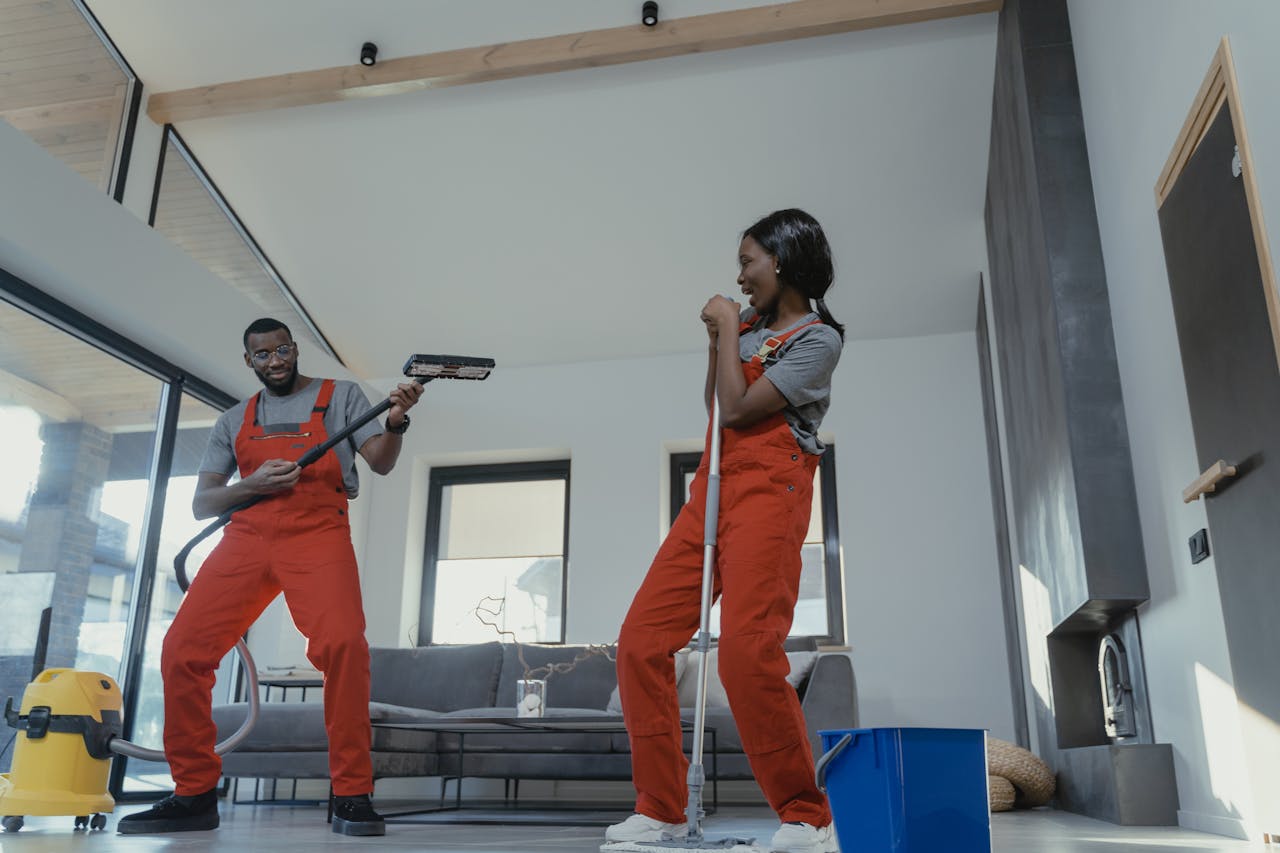 Two adults in vibrant coveralls cleaning a modern home interior, enjoying work.